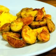 Breakfast potatoes on a white plate with some scrambled eggs alongside.