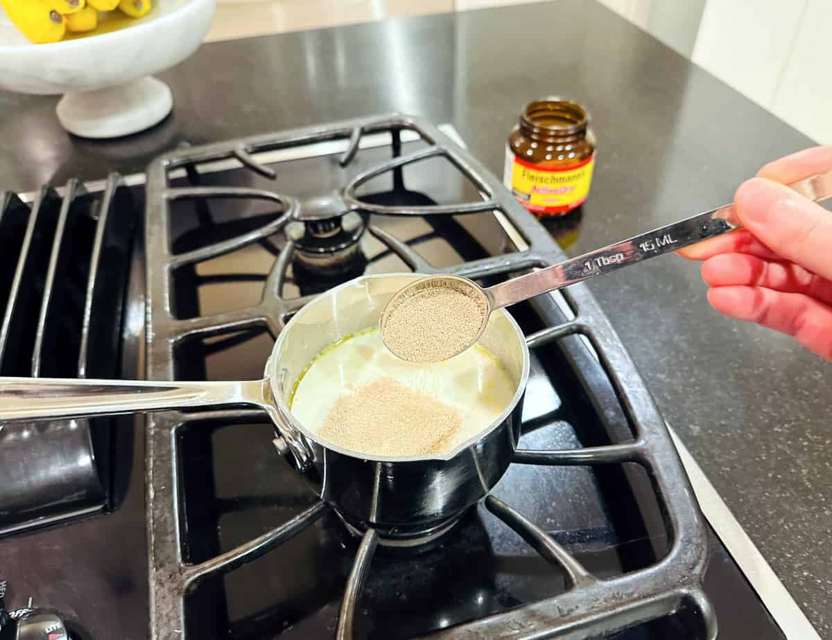 Yeast being tipped from a steel tablespoon into milk in a small steel saucepan.
