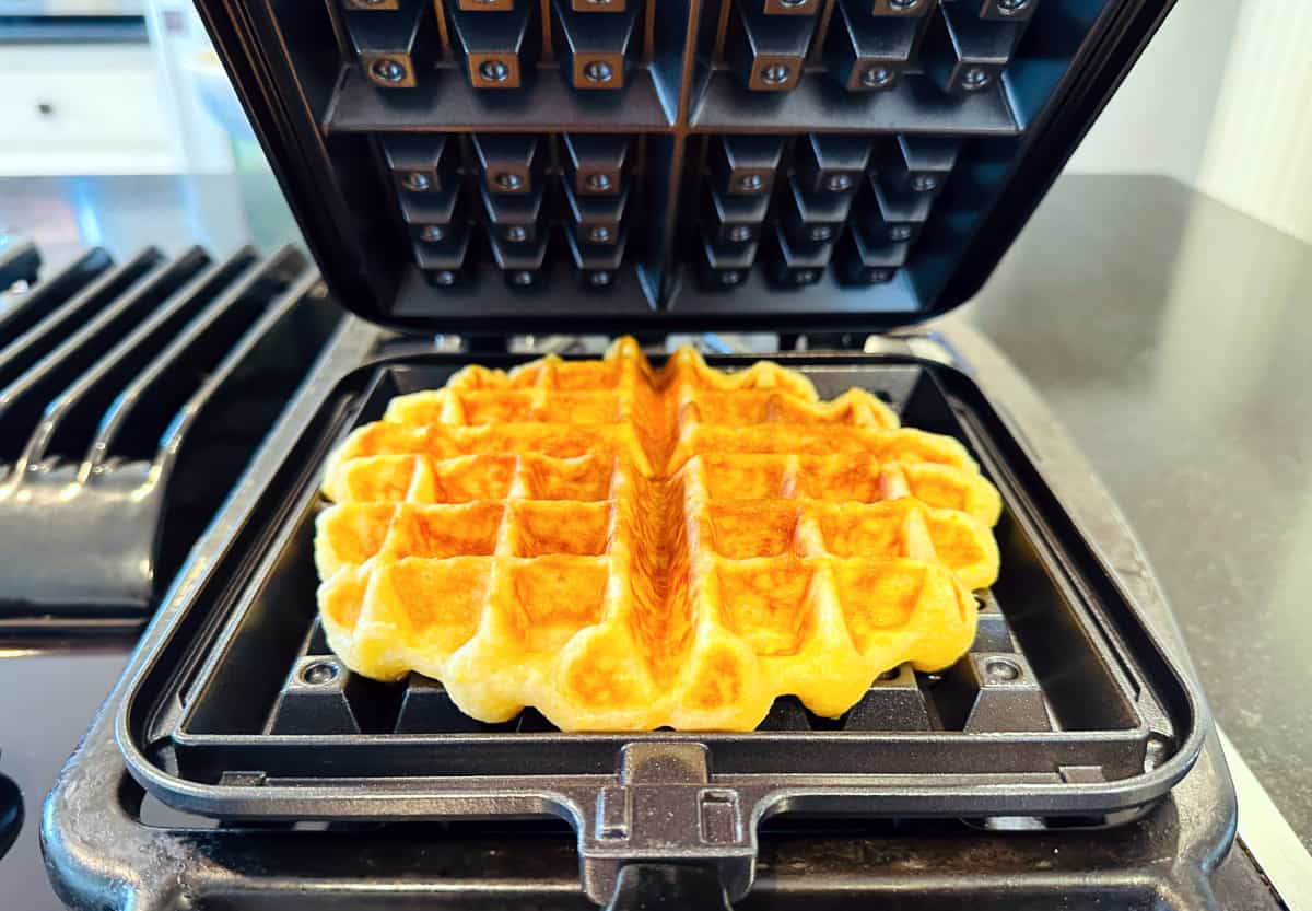 Homemade Belgian waffle cooking in a black waffle iron on the stove.
