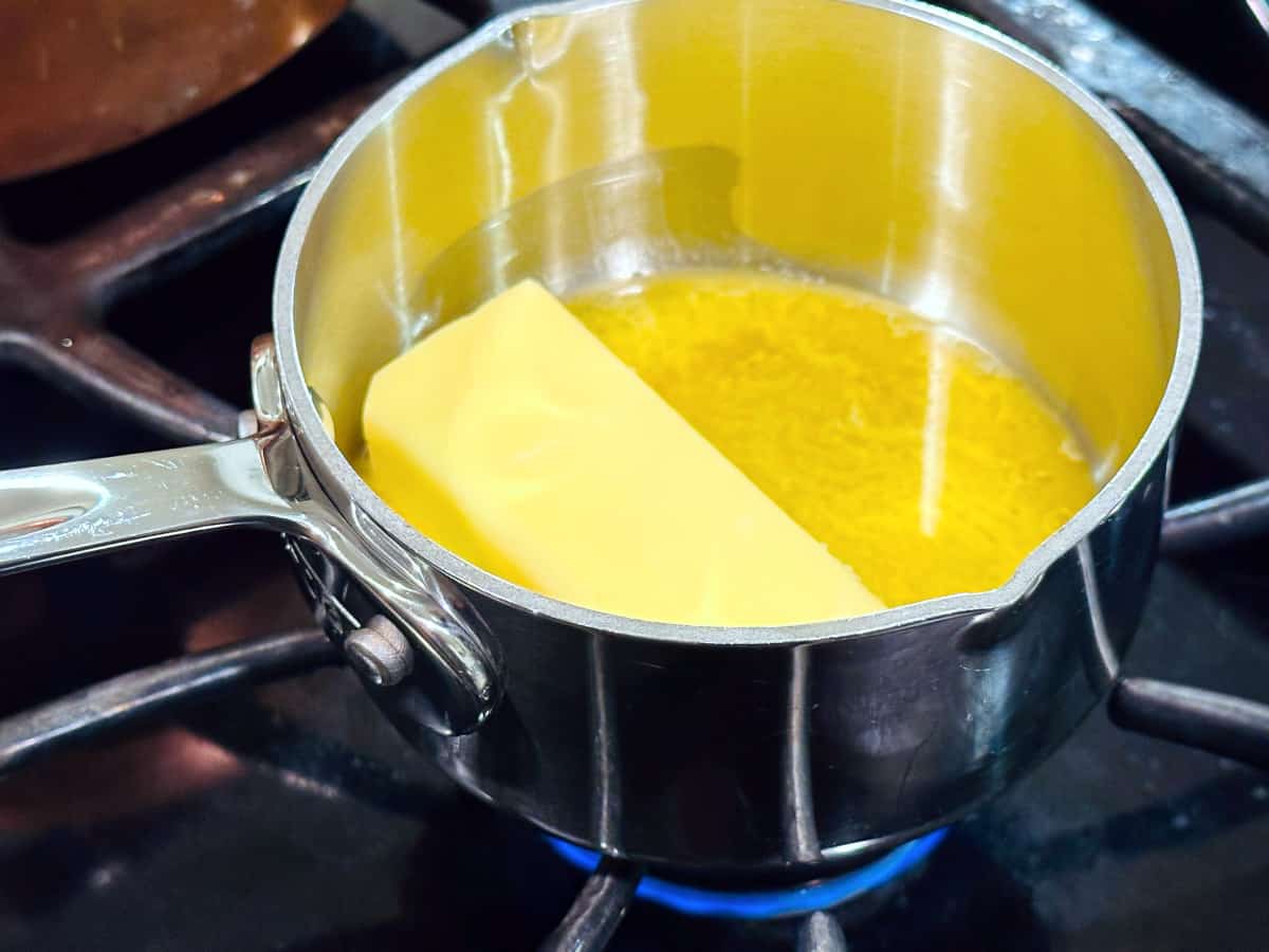 Stick of butter melting in a small steel saucepan on the stove.