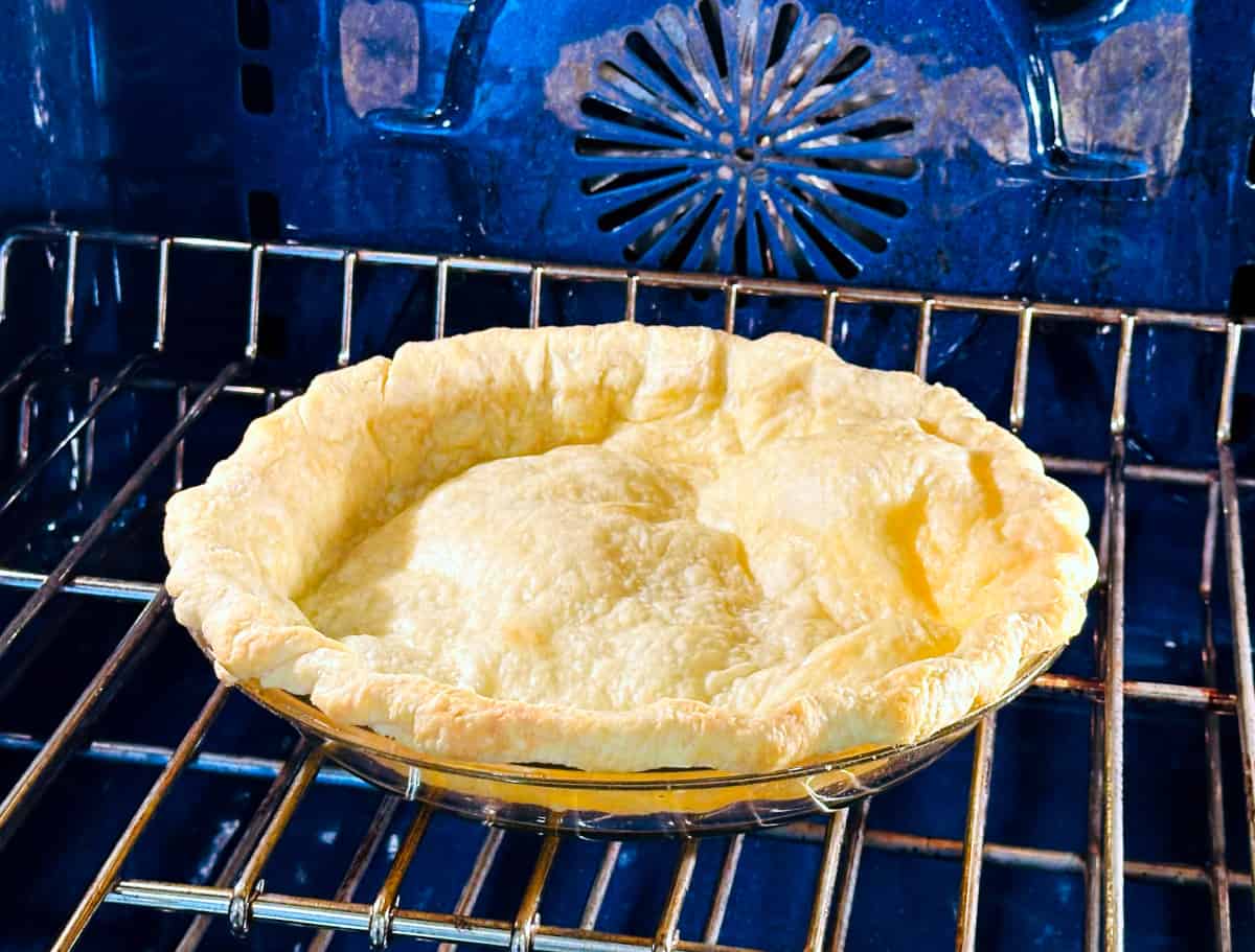 Empty pie crust baking in a blue oven.