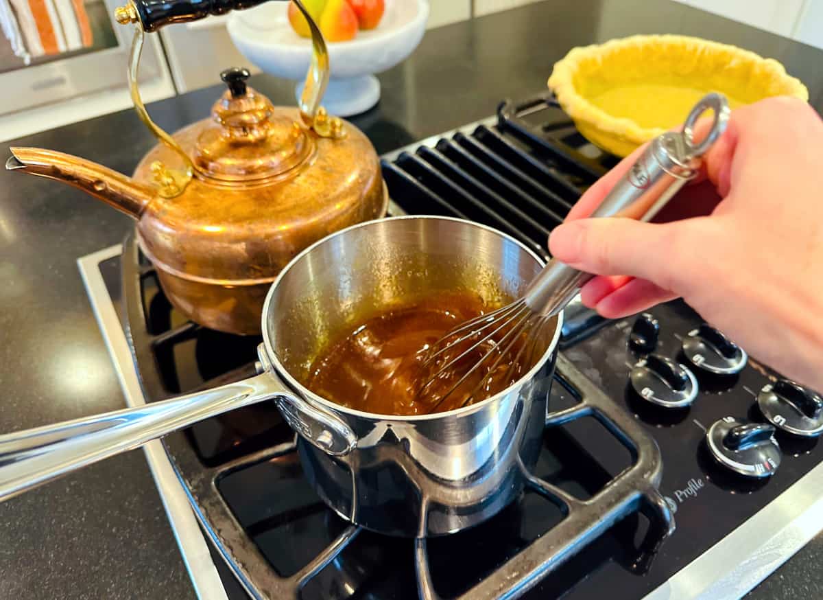 Brown liquid being stirred with a whisk in a steel saucepan on the stove.
