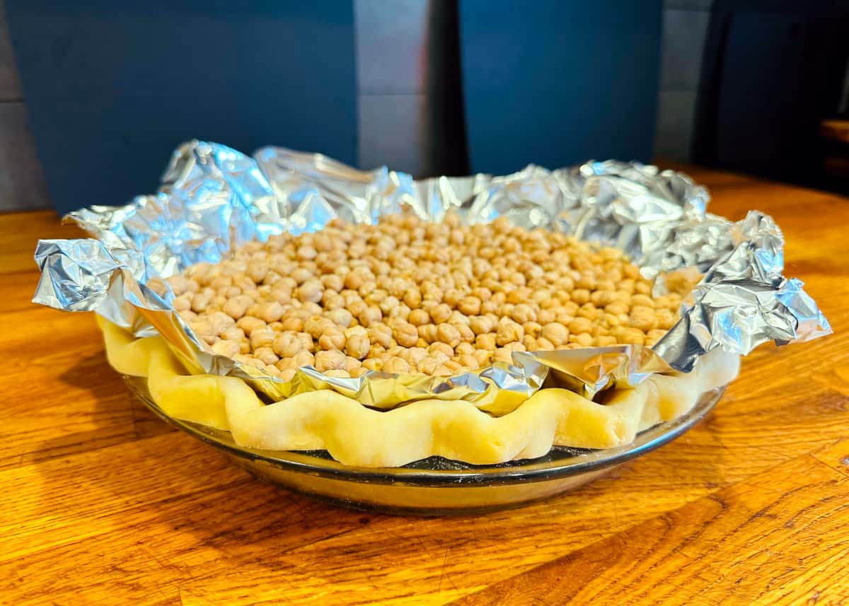 Unbaked pie crust lined with aluminum foil and filled with dried chickpeas.