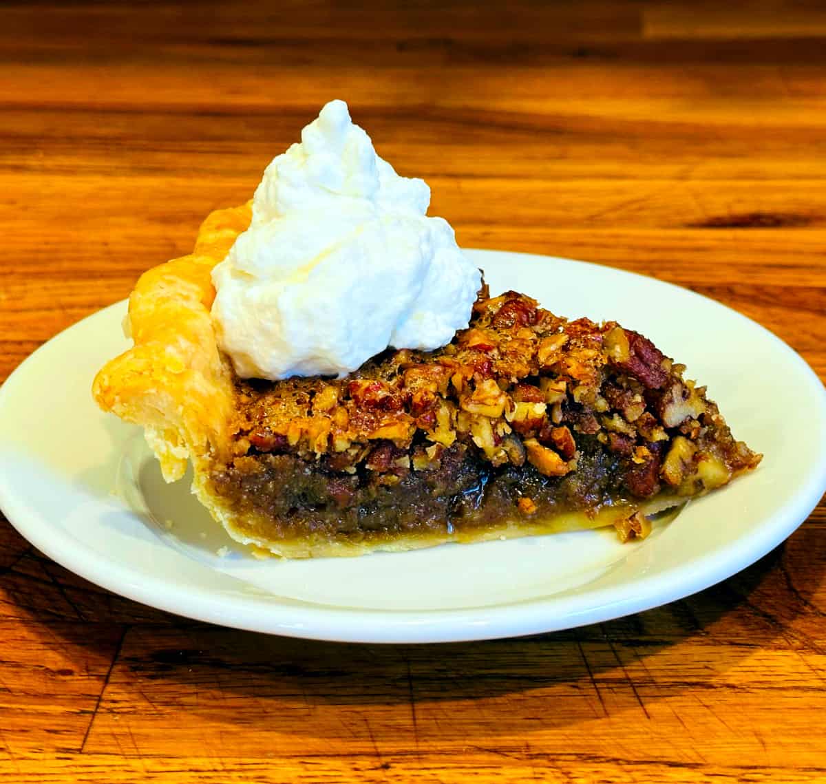 Slice of pecan pie on a small white plate with a big dollop of whipped cream on top.