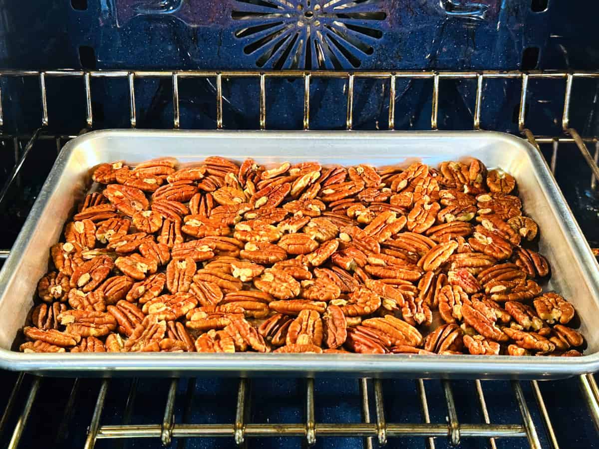 Whole pecans toasting on a rimmed baking sheet in a blue oven.