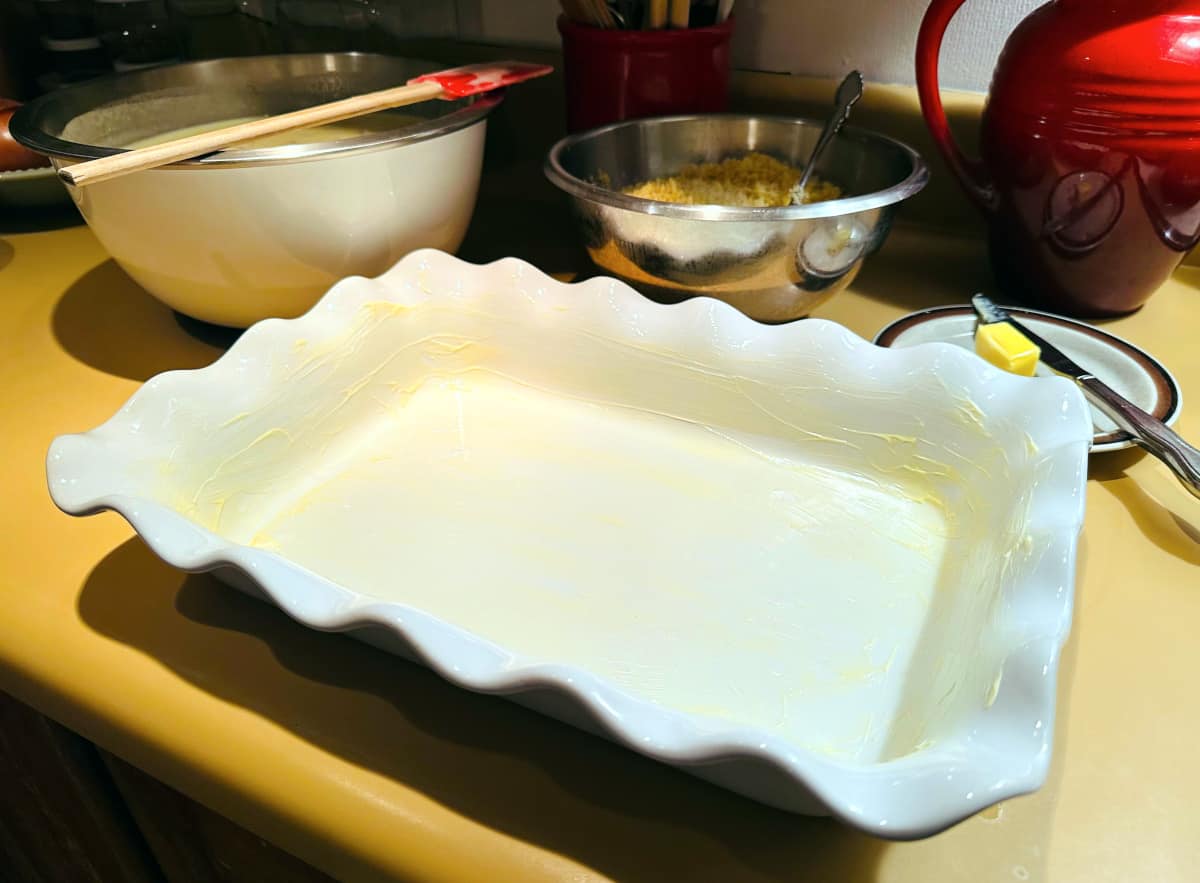 White baking dish with a white ruffled rim generously greased with butter.