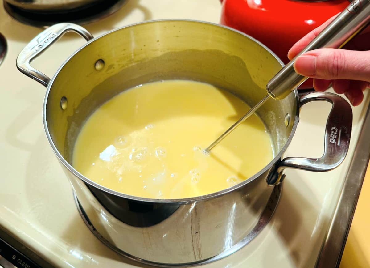 Pale yellow mixture of milk and roux being stirred together in a steel pot.