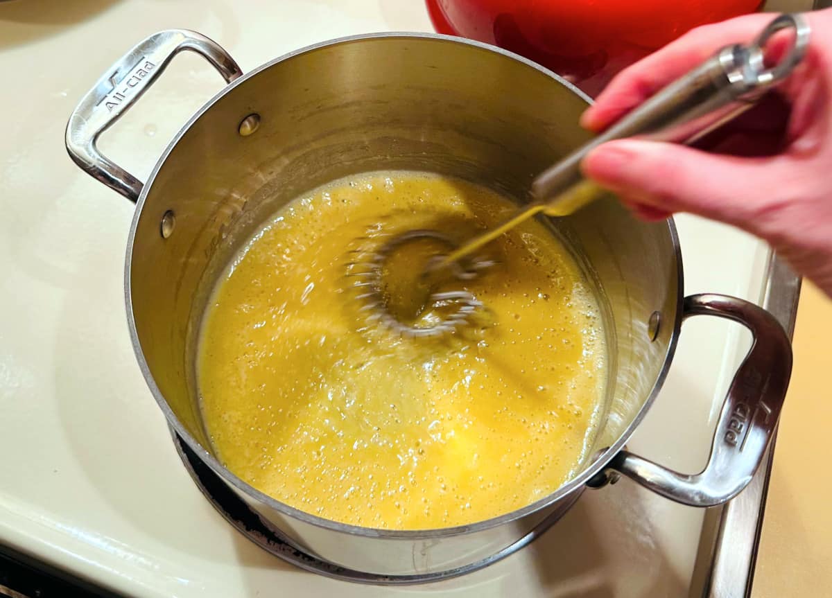 Pale yellow roux mixture being whisked in a steel pot.
