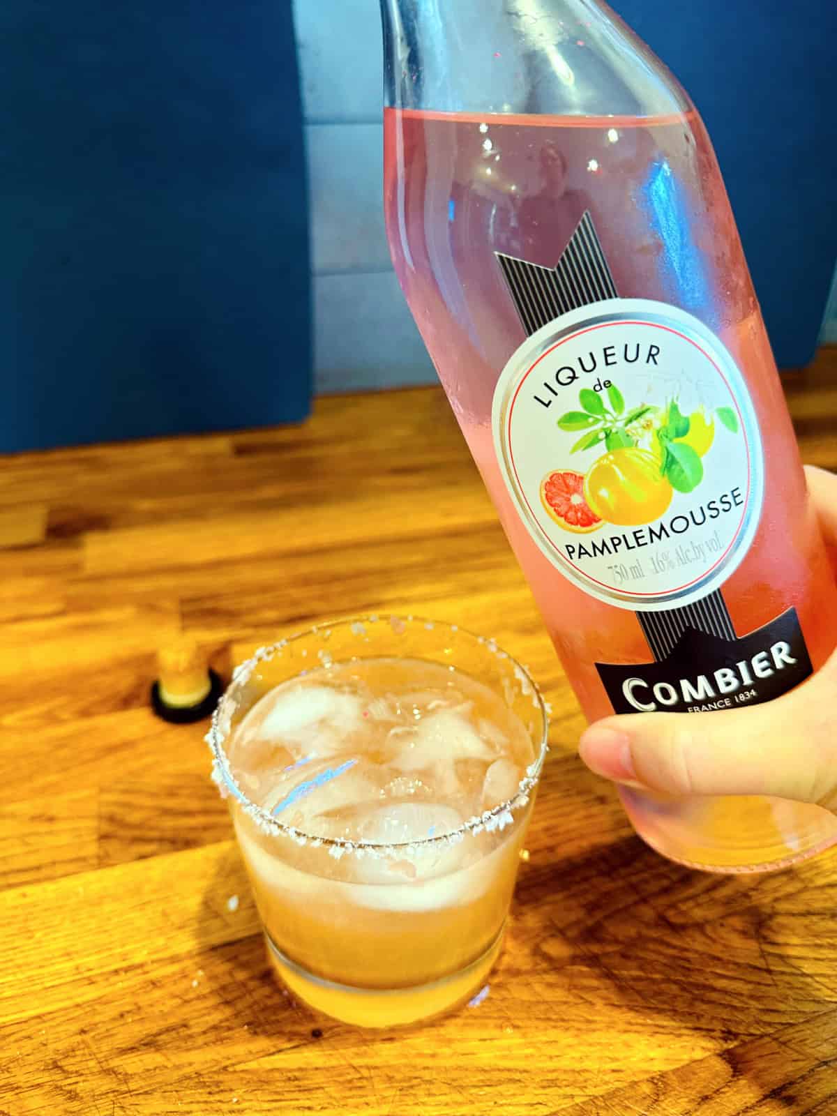 Bottle of pamplemousse liqueur being held next to a Paloma.