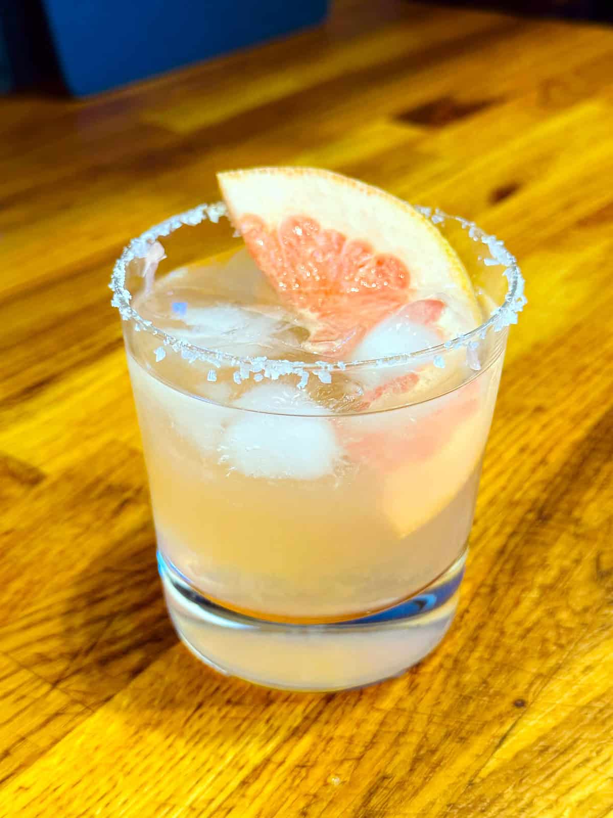 Paloma in an old fashioned glass with a salted rim and a large wedge of grapefruit.