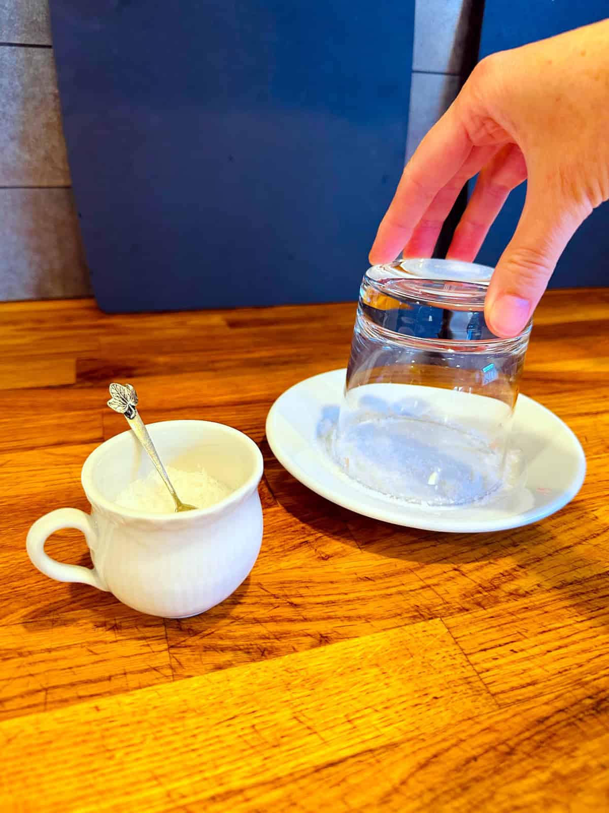 An old fashioned glass being turned upside down and dipped into salt on a small white plate.