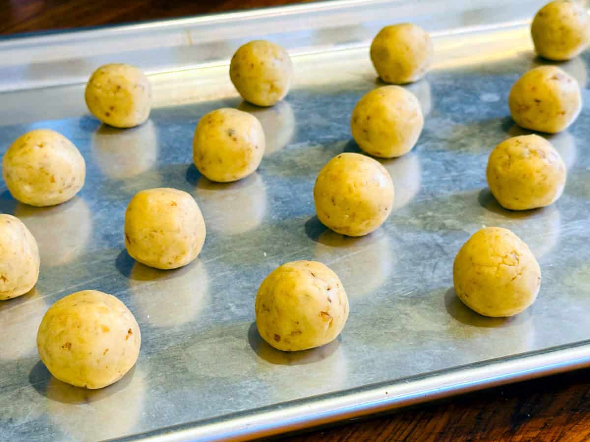 Pale yellow dough balls arranged on a metal baking sheet.