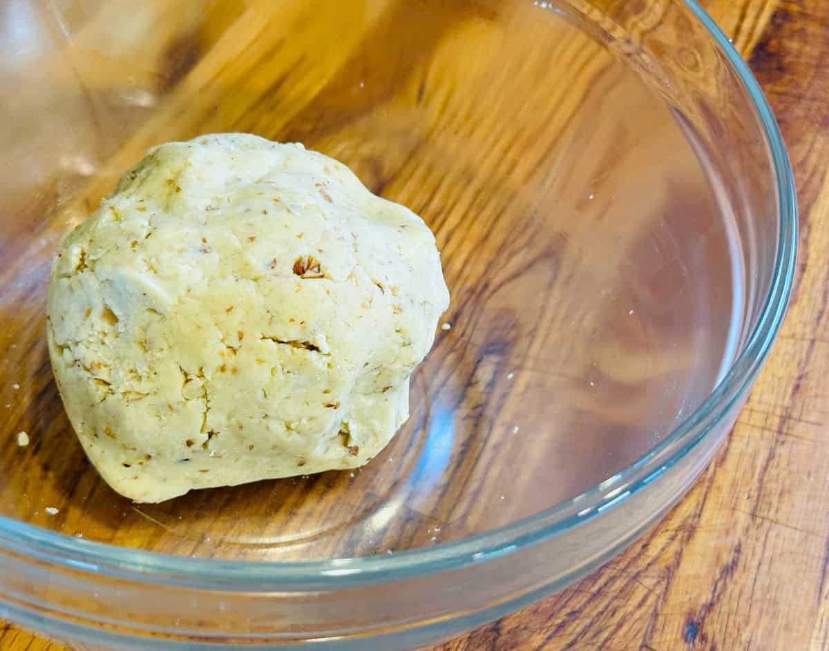 A large ball of pale yellow dough flecked with finely chopped walnuts in a glass bowl.