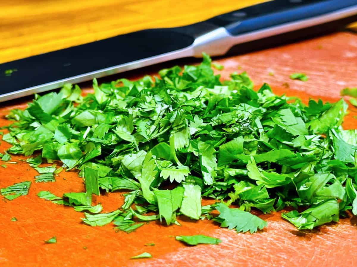 Chopped cilantro on a cutting board in front of a chef's knife.