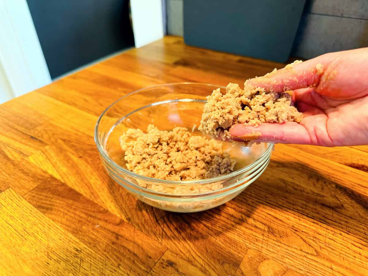 Light brown streusel topping being mixed by hand in a small glass bowl.