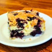 Slice of blueberry buckle served on a small white plate.