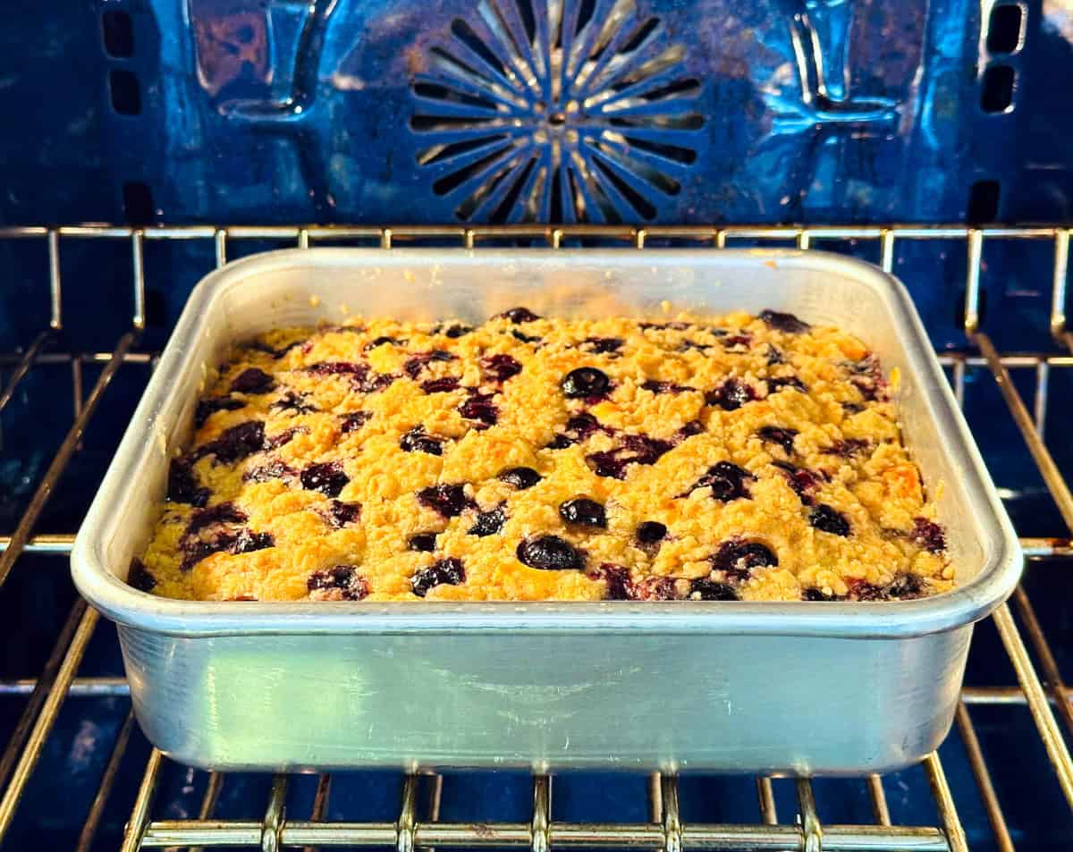 Blueberry buckle in a square metal pan baking in a blue oven.