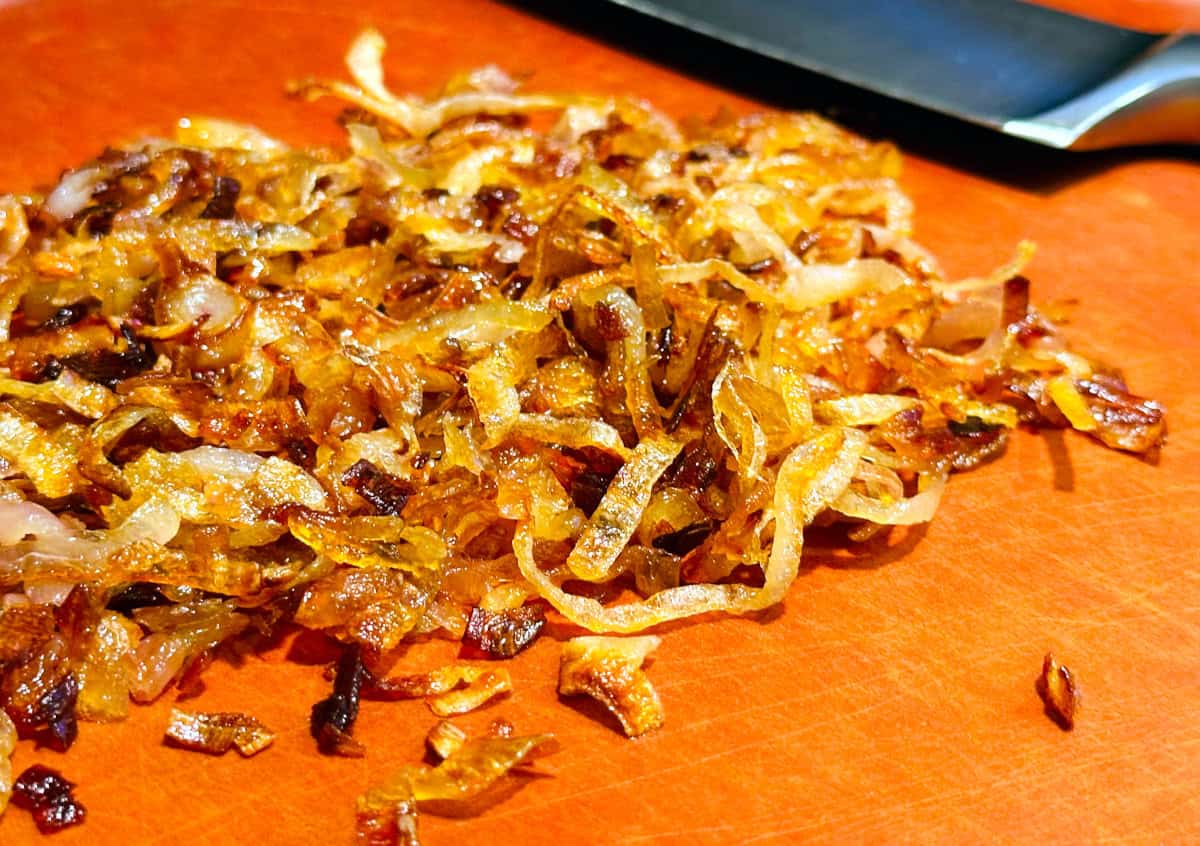 Fried shallots on a cutting board next to a chef's knife.