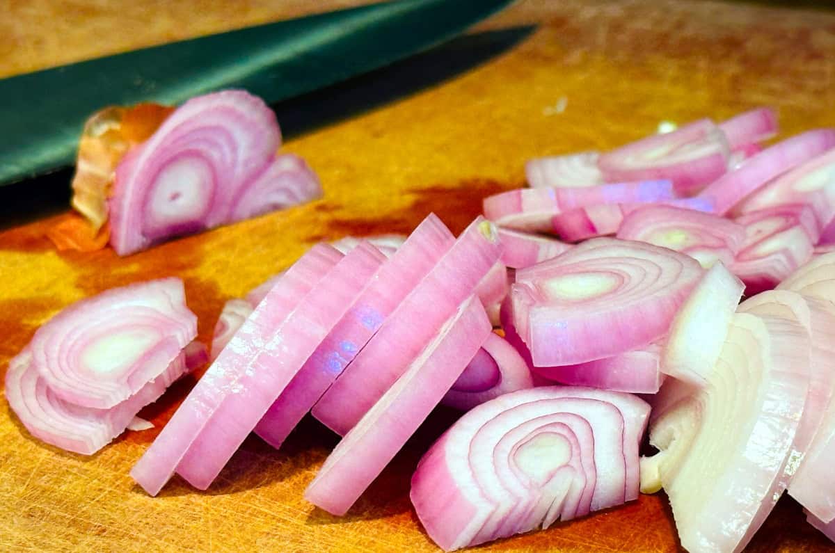 Chopped shallots on a cutting board next to a chef's knife.