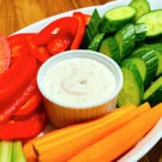 Shallot dip in a small white ramekin surrounded by raw chopped carrots, cucumbers, red pepper, and celery.