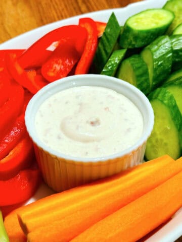 Shallot dip in a small white ramekin surrounded by raw chopped carrots, cucumbers, red pepper, and celery.