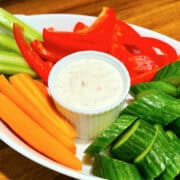 Shallot dip in a small white ramekin surrounded by raw chopped carrots, cucumbers, red pepper, and celery.