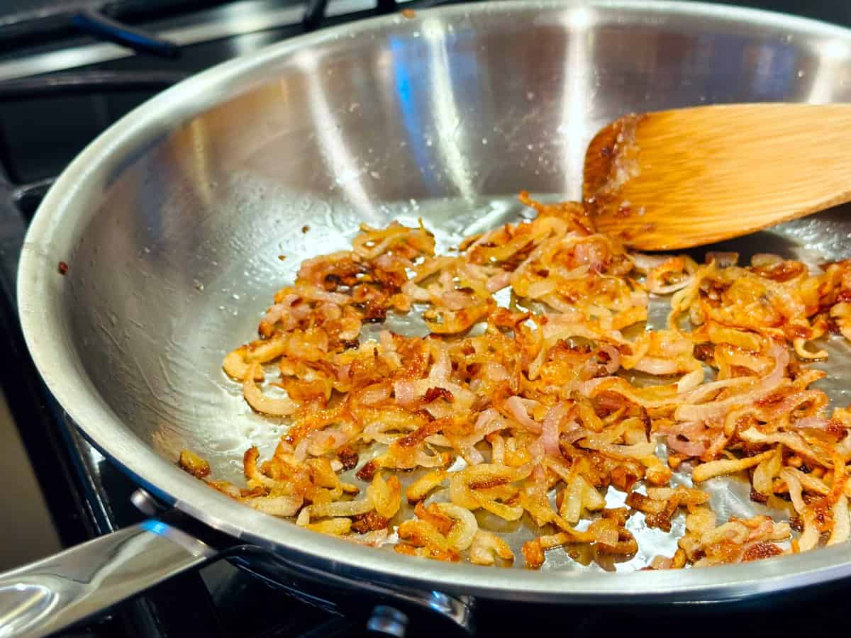 Chopped shallots frying in a medium steel skillet.