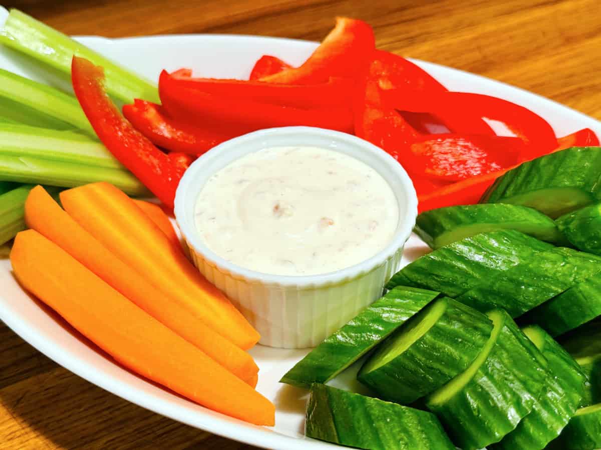 Shallot dip in a small white ramekin surrounded by raw chopped carrots, cucumbers, red pepper, and celery.