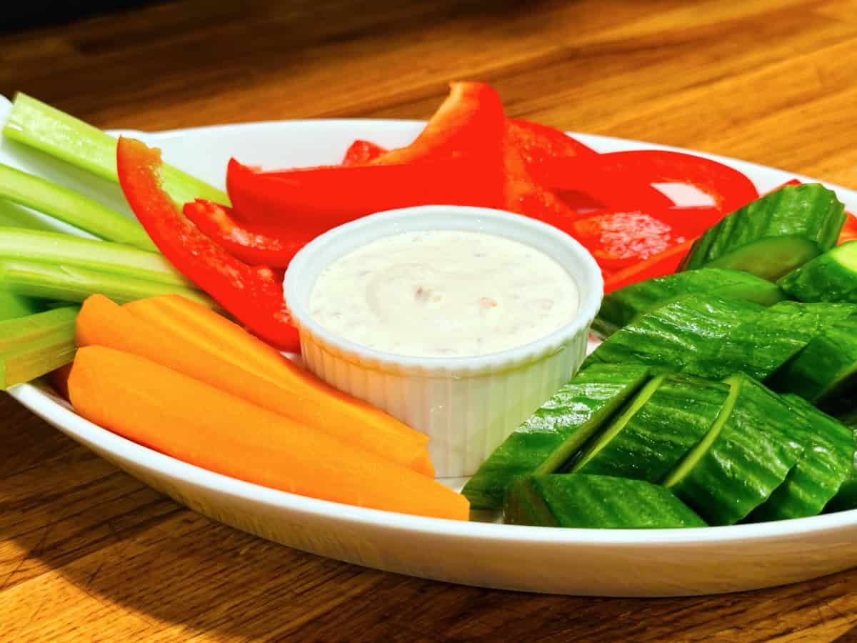 Shallot dip in a small white ramekin surrounded by raw chopped carrots, cucumbers, red pepper, and celery.