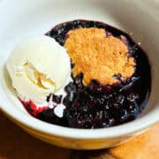 Blueberry cobbler with a scoop of vanilla ice cream in a white bowl.