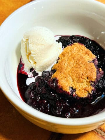 Blueberry cobbler with a scoop of vanilla ice cream in a white bowl.