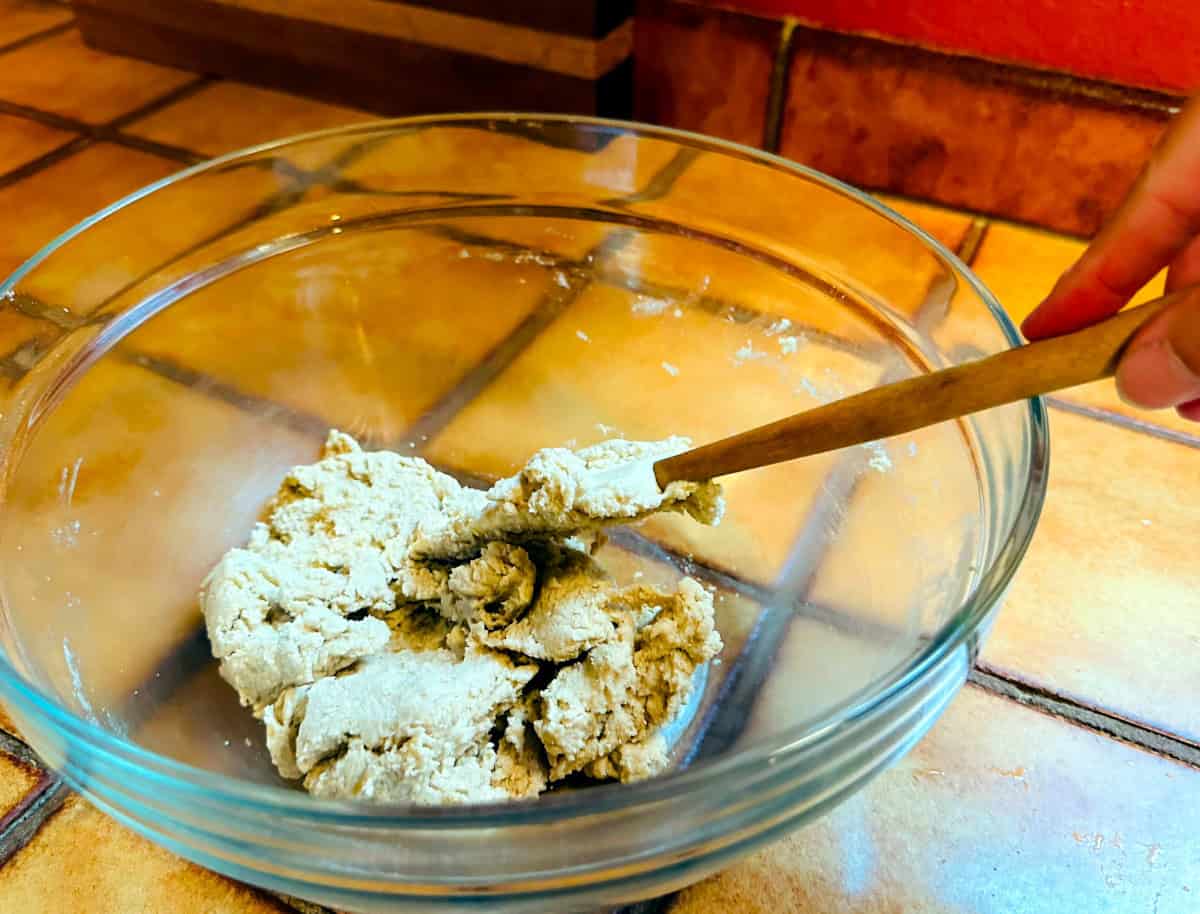 Biscuit topping dough being mixed with a silicone spatula in a glass bowl.