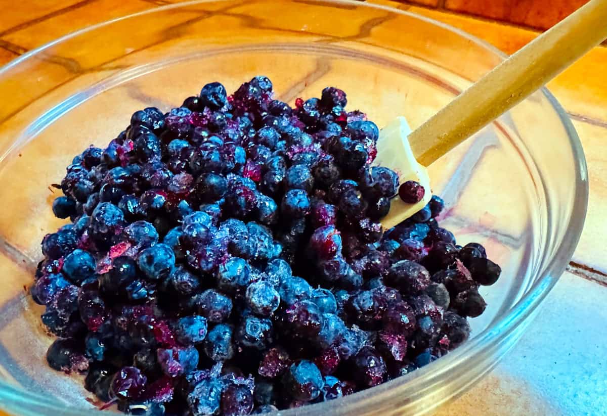 Blueberries being stirred with a silicone spatula in a glass bowl.