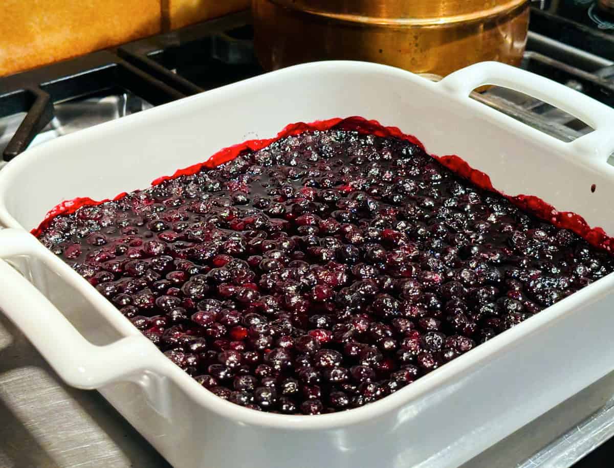 Cooked blueberries in a square white baking dish sitting on the stove.