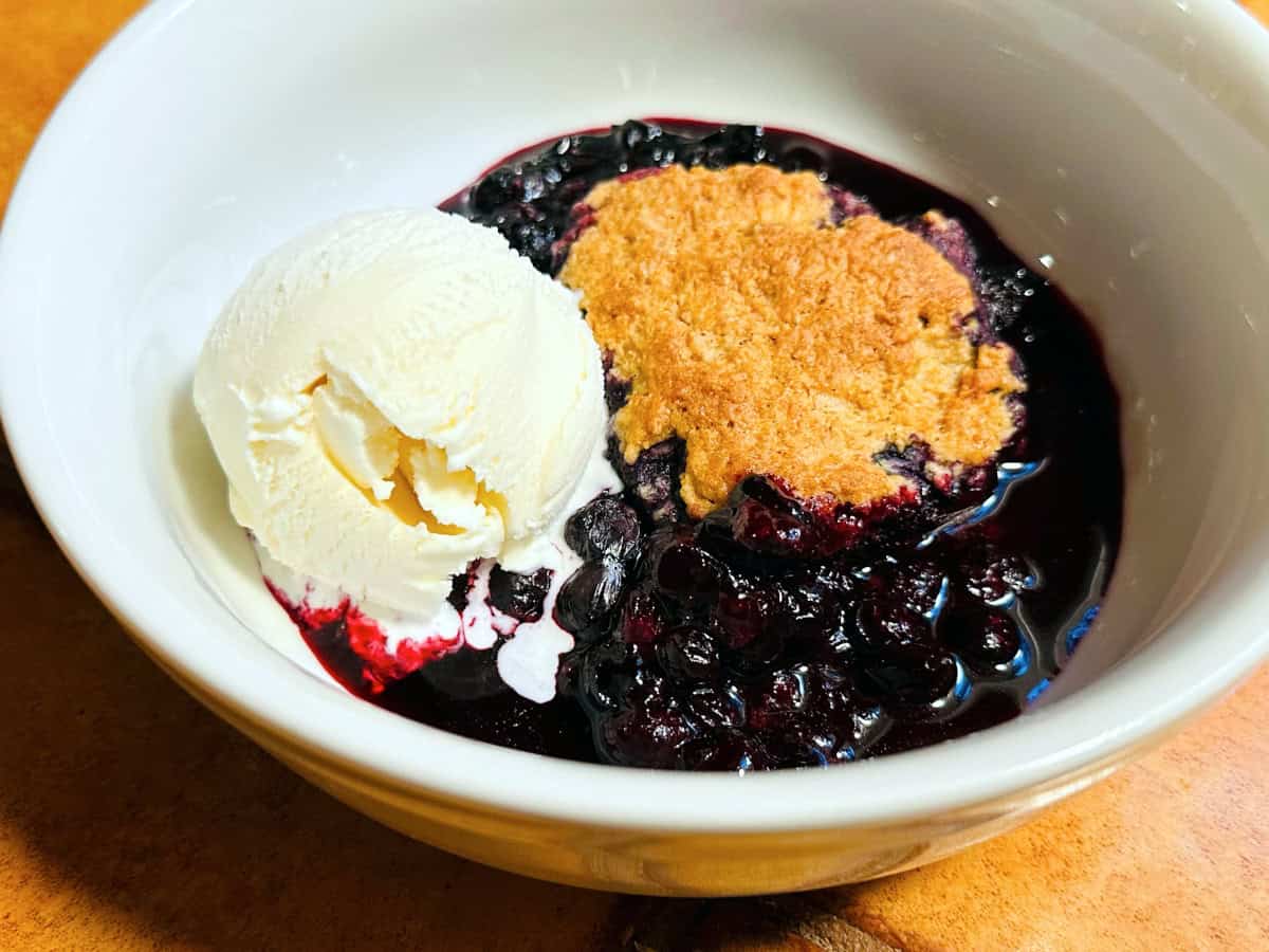 Blueberry cobbler with a scoop of vanilla ice cream in a white bowl.