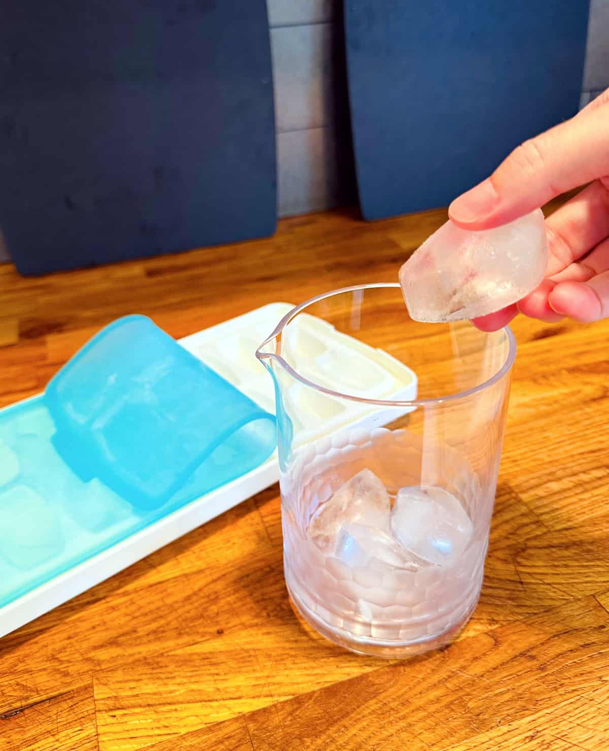 Ice being dropped into a mixing glass next to a white and blue ice cube tray.