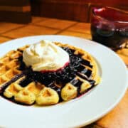 Lemon poppy seed waffle topped with blueberry sauce and whipped cream on a white plate.