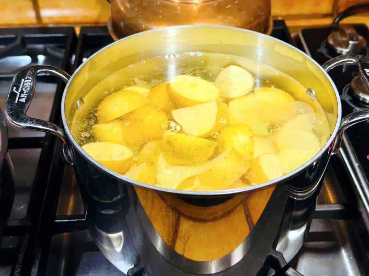 Potato chunks cooking in simmering water in a steel pot sitting on the stove.