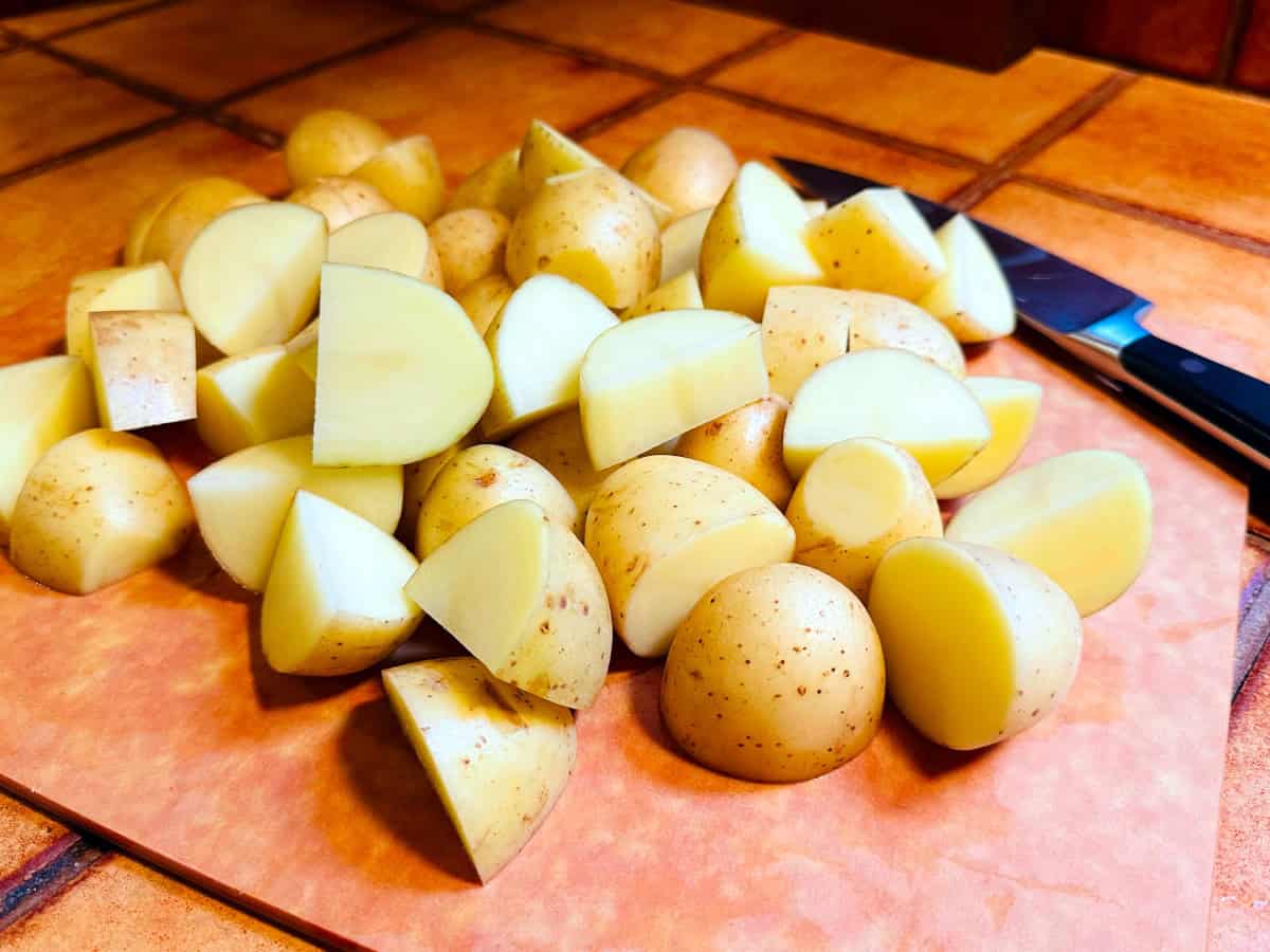 Raw potato chunks on a cutting board with a chef's knife.