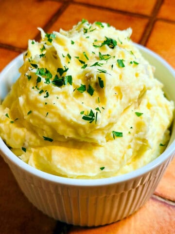 Creamy mashed potatoes with chopped parsley sprinkled on top in a white ridged soufflé dish.