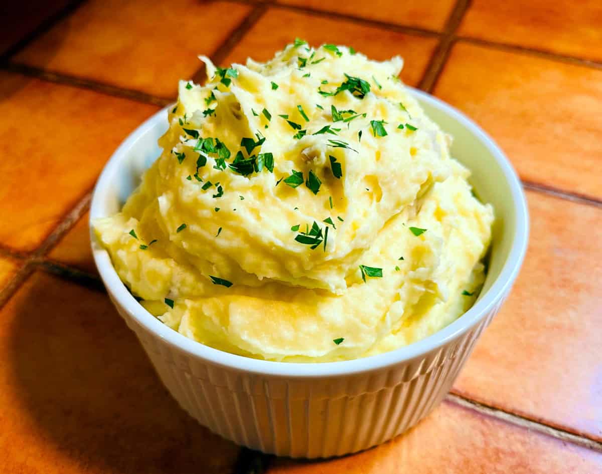 Creamy mashed potatoes with chopped parsley sprinkled on top in a white ridged soufflé dish.