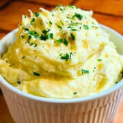 Creamy mashed potatoes with chopped parsley sprinkled on top in a white ridged soufflé dish.