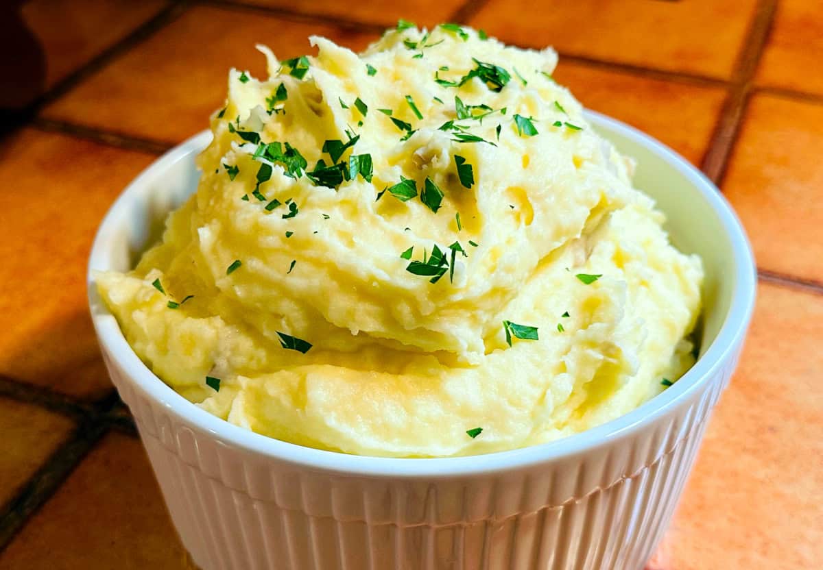 Creamy mashed potatoes with chopped parsley sprinkled on top in a white ridged soufflé dish.