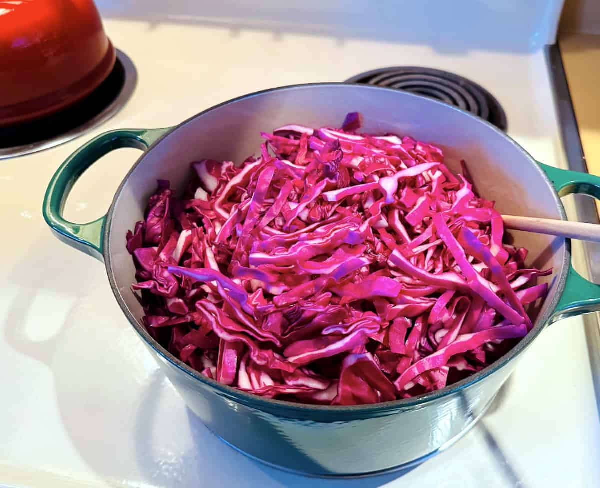 Raw chopped red cabbage in a dark green dutch oven on the stove.