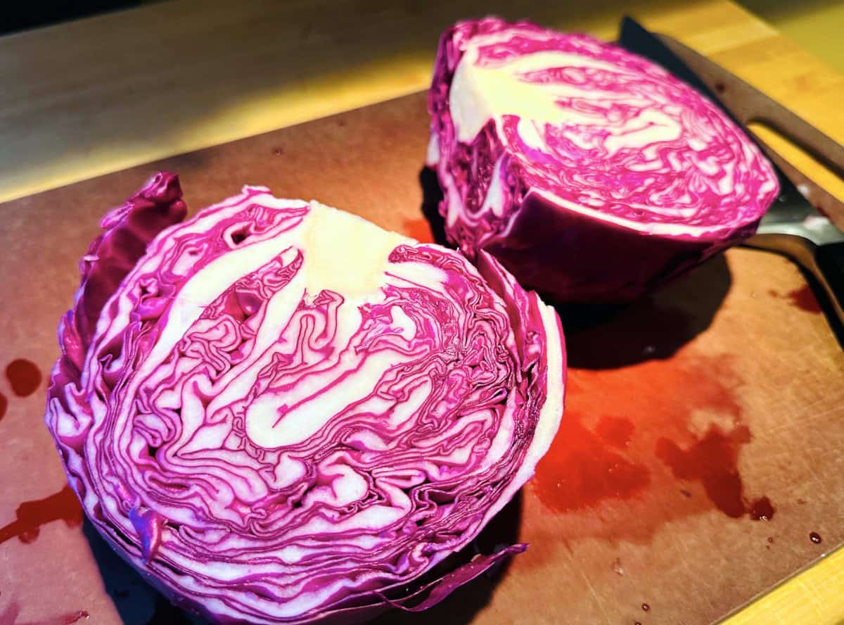 Two halves of a red cabbage sitting on a cutting board.