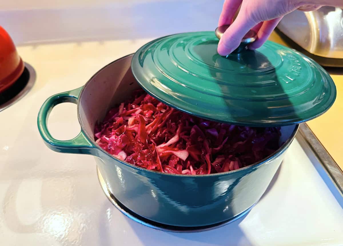 German red cabbage in a dark green dutch oven with the lid halfway on.