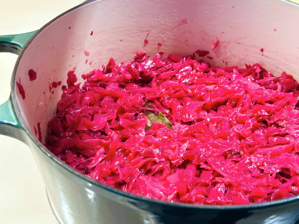 Bright purple cooked cabbage with a bay leaf in a dark green dutch oven.