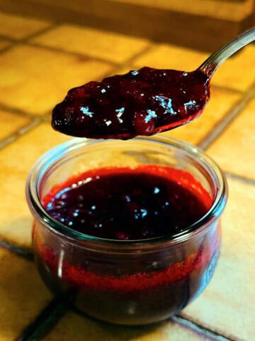 Spoonful of lingonberry sauce being held over a jar of lingonberry sauce.