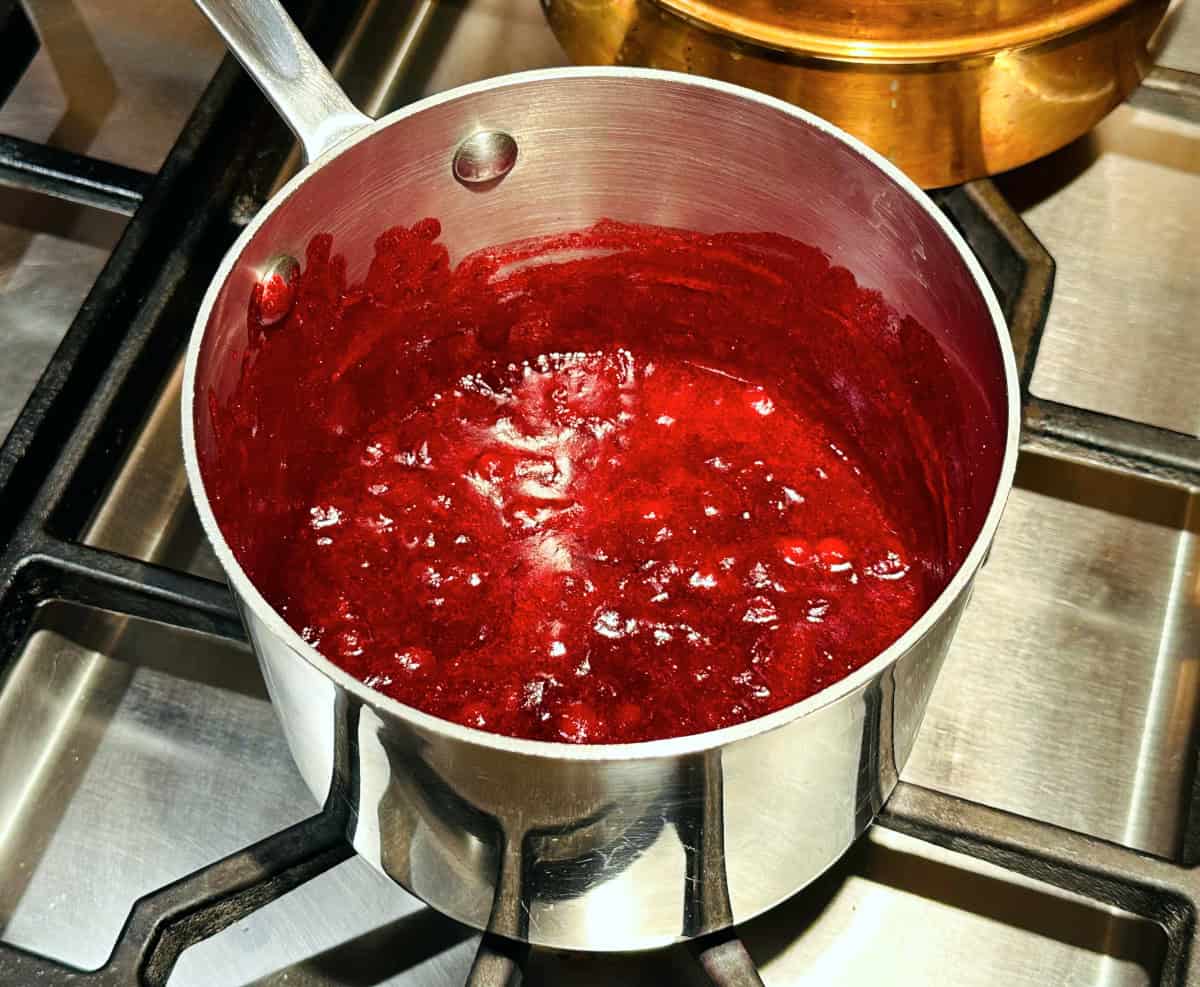 Dark red berry sauce in a small steel saucepan sitting on the stove.