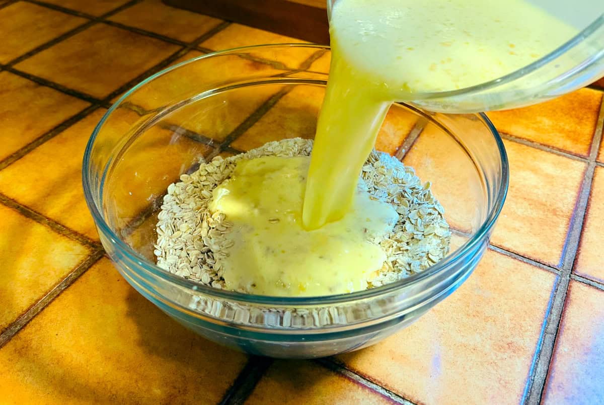 Pale yellow liquid being poured from one glass bowl into another glass bowl containing dry ingredients.